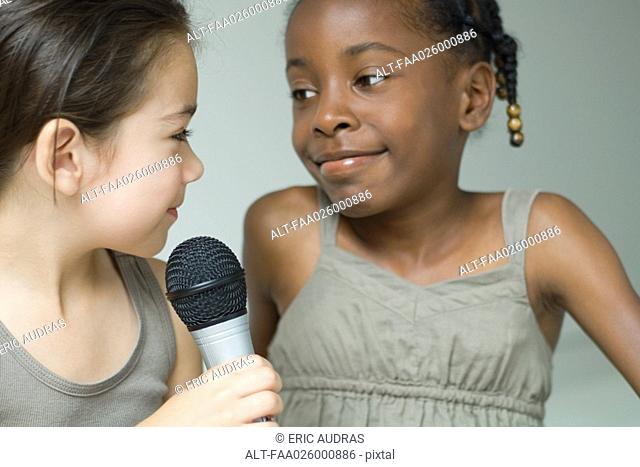 Two little girls smiling at each other, one holding microphone, close-up