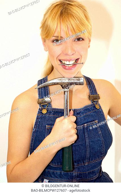 young DIY woman in overalls with hammer and nail