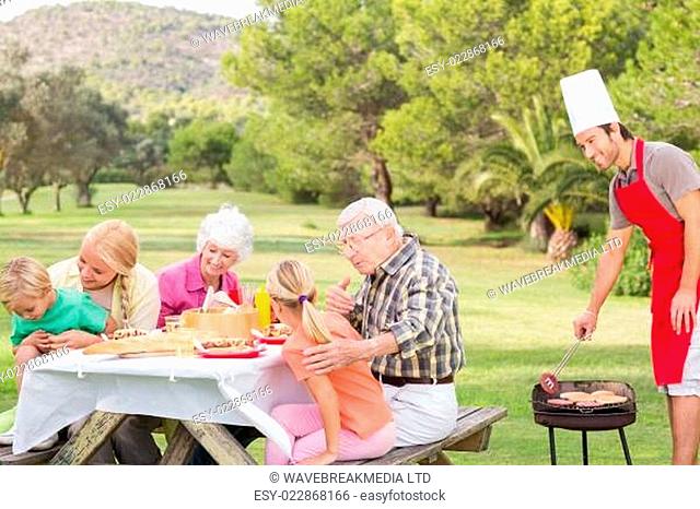 Happy family at picnic table with father at the barbeque in the park