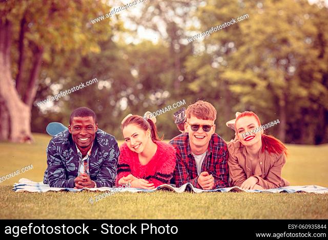 Beautiful people spending their free time with nature. Picture of happy couples smiling to camera while lying on picnic rug on picnic