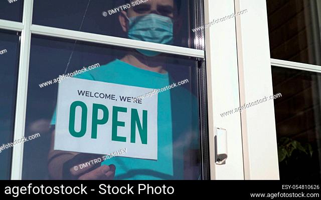 Close up of the male Caucasian hands turning a signboard on the glass door of the shop from CLOSED to OPEN. Reopening of a small business activity after...