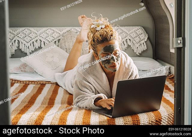 Pretty adult woman with skin beauty cream on face work on laptop computer laying in camper van bedroom. Travel lifestyle female people with online job