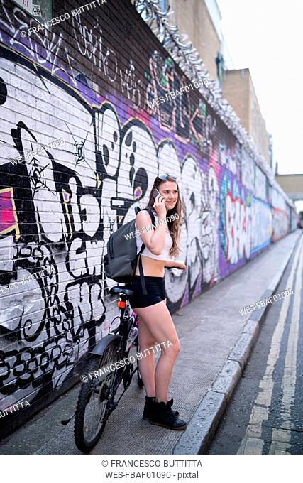 Smiling young woman on the phone at graffiti wall