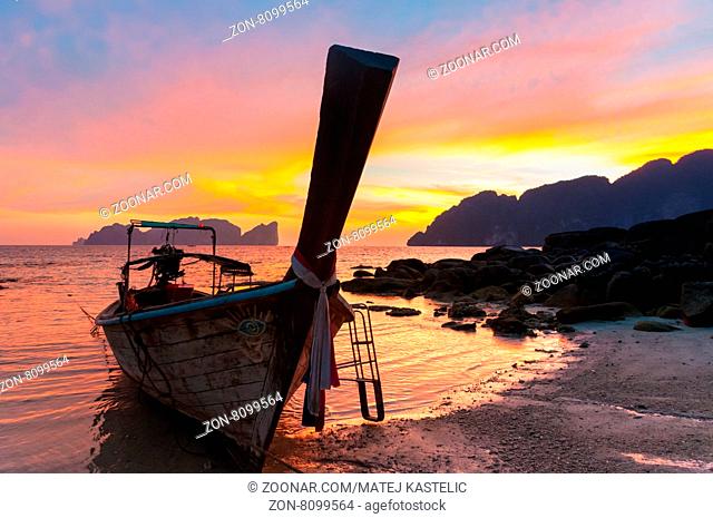 Traditional thai wooden longtail boat on beach of Phi-Phi Don island in sunset. Silhouette of famous Phi Phi Lee island in background