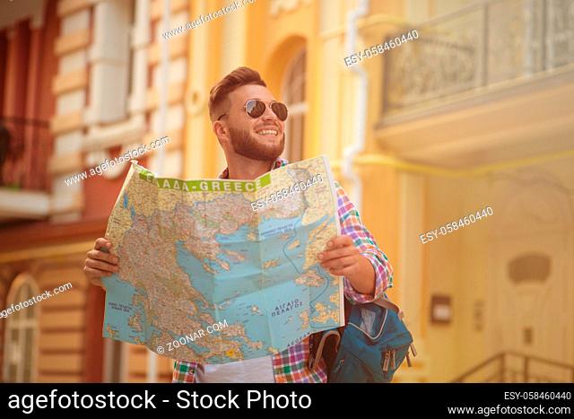 European hipster man in sunglasses smiling and carrying a guide in his hands. Bearded man with backpack going to visit all the city's sightseeings