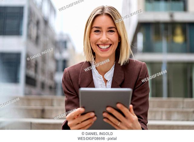 Portrait of happy young businesswoman using tablet in the city