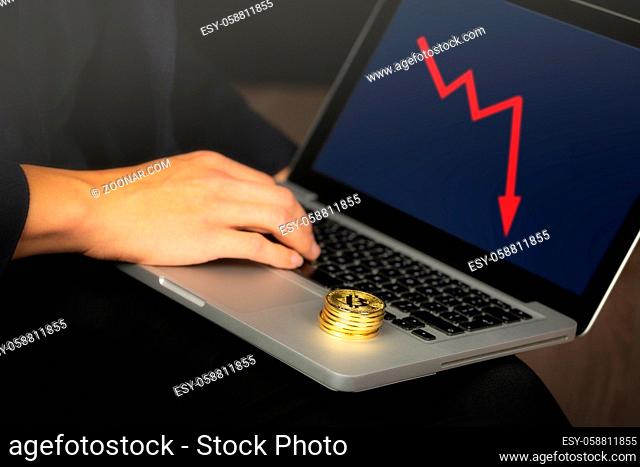 Businessman working on laptop with a golden bitcoin coins stack on it. Red chart, price crash concept