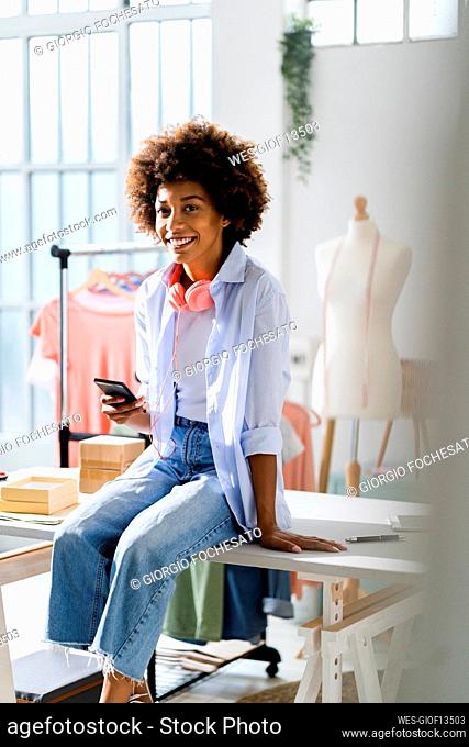Smiling businesswoman with smart phone sitting on desk at studio