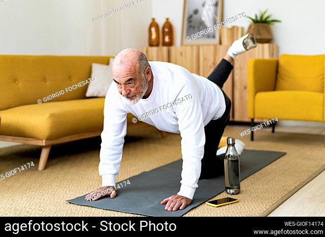 Fit senior man practicing Bharmanasana yoga pose at home