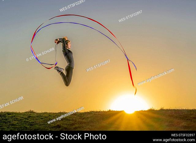 Female gymnast practicing with ribbons over land during sunset