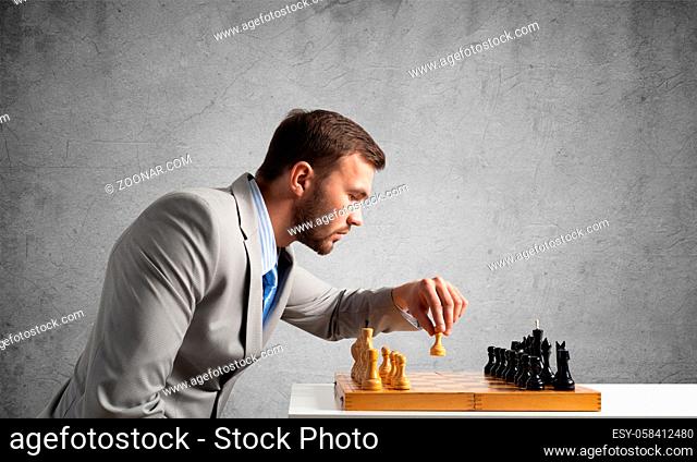 Businessman moving chess figure in chessboard. Successful management and leadership. Handsome man in business suit at desk with chess on grey wall background
