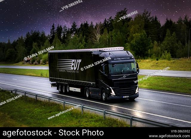New, black Volvo FH semi trailer truck Euroopa Transpordi OU transporting goods on motorway under starry sky at night. Composite image. Finland, 2021
