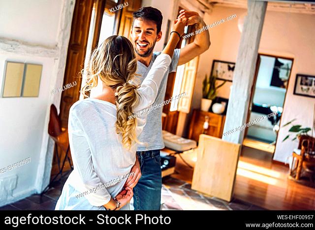 Happy young couple dancing in living room at home