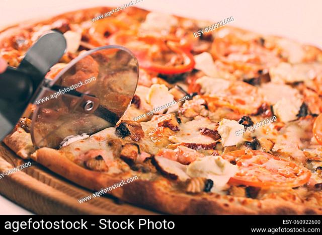 Closeup hand of chef baker in white uniform cutting pizza at kitchen