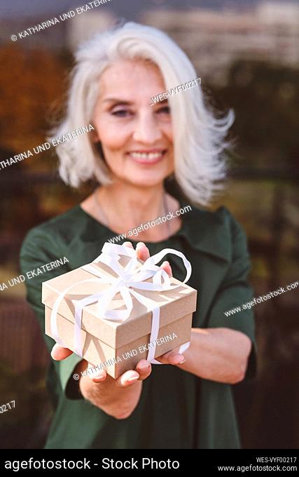 Smiling mature woman holding gift while standing at restaurant