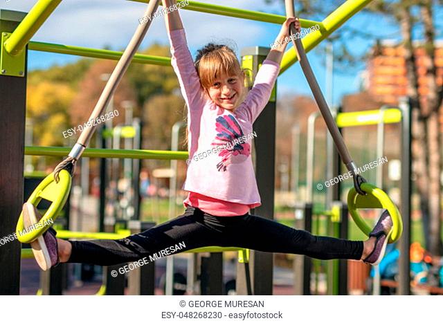 Young girl stretches in splits position on gymnastic rings outside on a playground