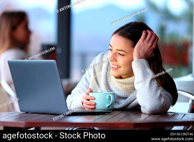 Happy woman in winter watching media on laptop in a bar terrace