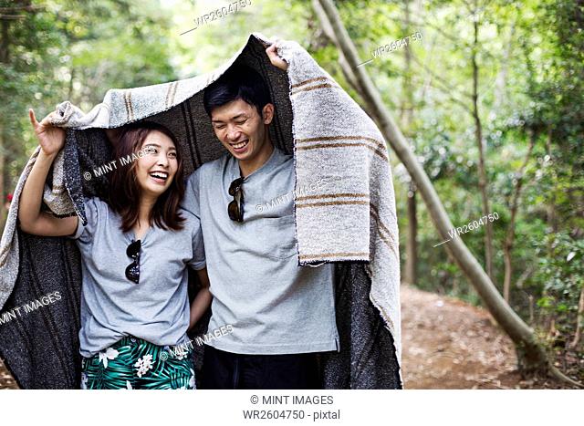 Young woman and man standing in a forest, holding a blanket over their heads