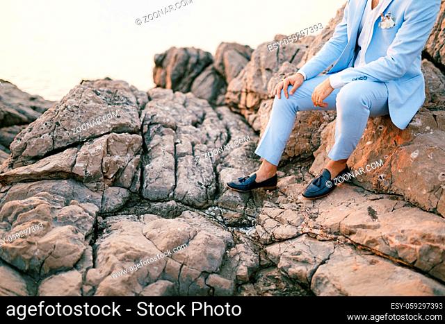 A man in a blue suit with a boutonniere and moccasins sits on the rocks . High quality photo