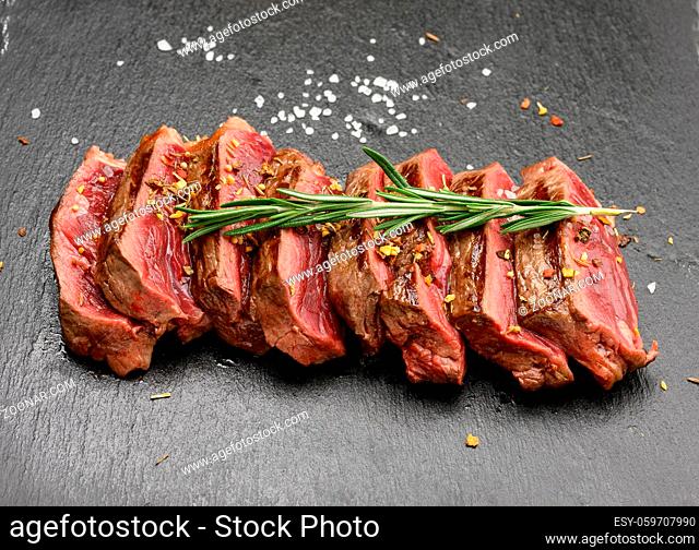 sliced fried beef steak New York striploin on a black background with spices, degree of doneness rare, close up