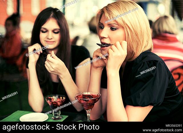 Two young women eating dessert at sidewalk cafe