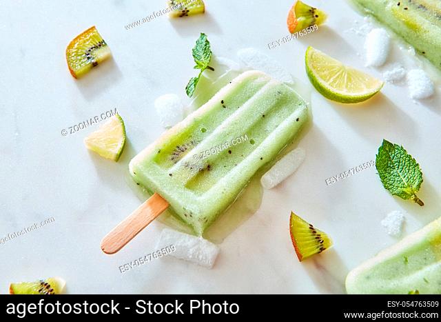Fruit frozen juice lolly. Summer composition of a refreshing ice cream with ice, mint leaves, pieces of kiwi and lime on a gray marble background with space for...