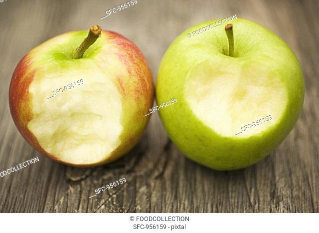 Two apples with bites taken on wooden background