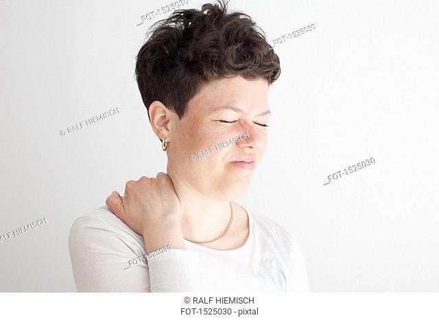Close-up of mid adult woman suffering from shoulder pain against white background