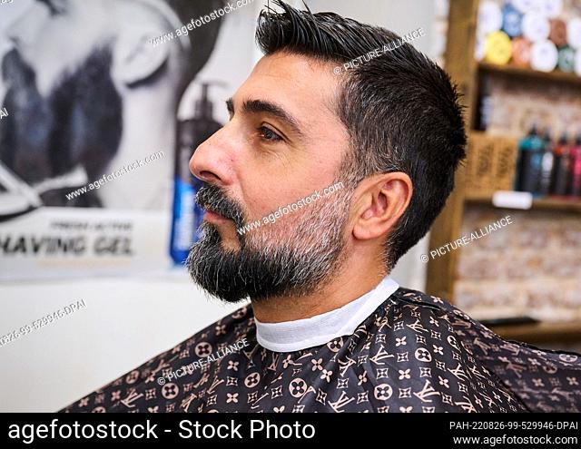24 August 2022, Berlin: A man wears a full beard while sitting at the barber wearing a cape. (To dpa: ""Hairy thing: records and interesting facts about...
