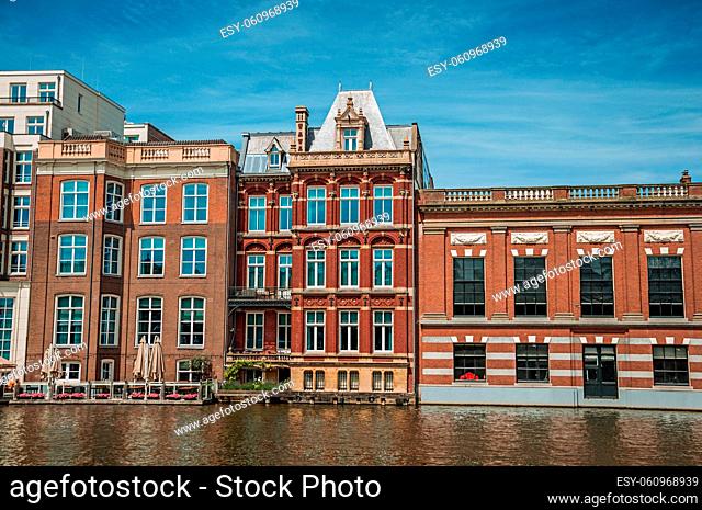Old brick buildings facade and restaurant along the canal and sunny blue sky in Amsterdam. The city is famous for its huge cultural activity