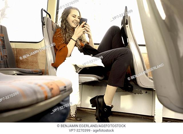 young woman sitting in public transport, using phone, happy laughing, in city Cottbus, Brandenburg, Germany