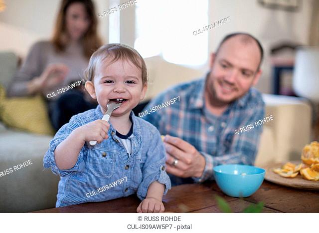 Baby boy feeding himself with spoon looking at camera smiling