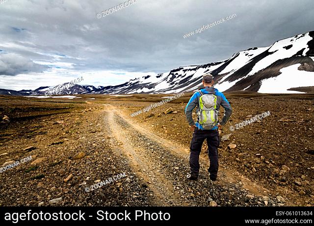 Young Man with Backpack hiking on dirt road trail in arctic desert and snow mountains of Iceland. Kaldidalur, Thorisjokull, Iceland
