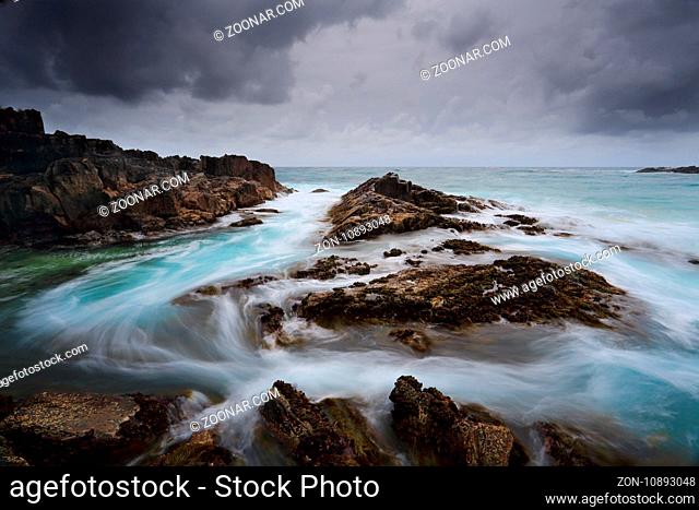 Heavy storm clouds loom overhead as fast flowing water moves swiftly through the channel. Location Meringo, Australia