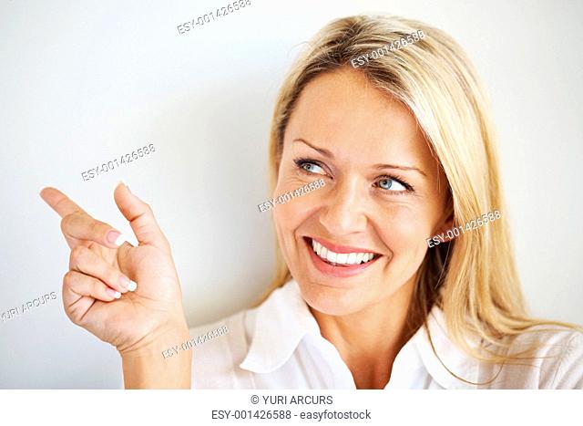 Closeup portrait of smiling young woman pointing at copyspace against grey background
