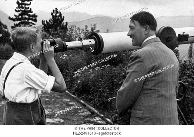 Adolf Hitler at his residence in Obersalzberg, Bavaria, Germany, 1936. Hitler (1889-1945) with a boy looking through a telescope at the Nazi leader's mountain...
