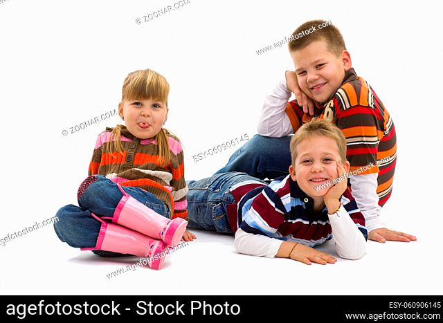 Group of 3 happy children lying on floor wearing colorful, trendy clothes, smiling. Isolated on white background