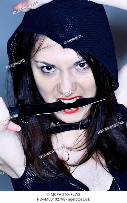 Young gothic woman with a knife between her teeth