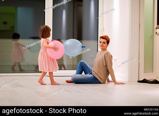 happy family spending time together young redhead mother and cute little daughter having fun while playing with balloons near the window on beautiful evening at...