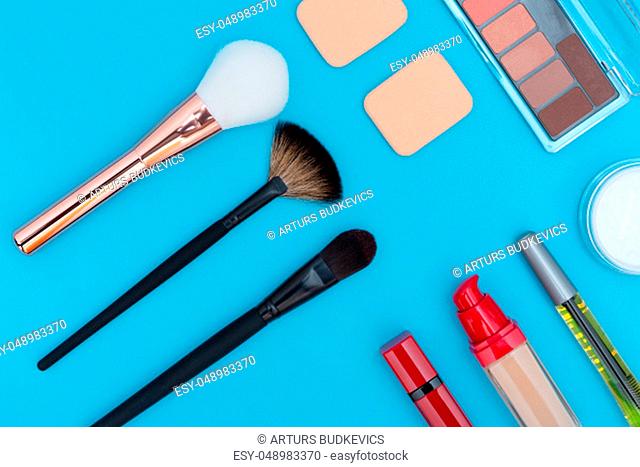 Decorative cosmetics, makeup products and brushes on blue background