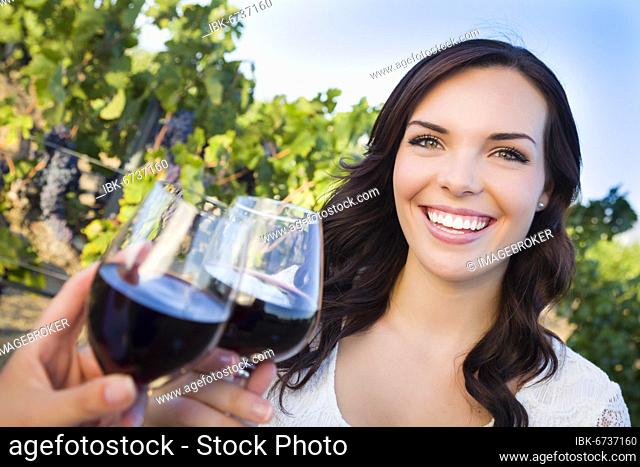 Pretty mixed-race young adult woman enjoying A glass of wine in the vineyard with friends