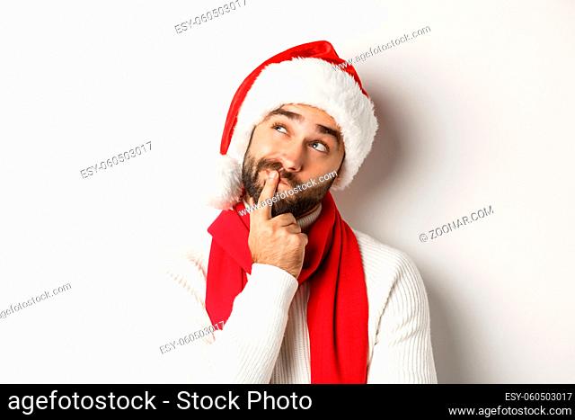 New Year party and winter holidays concept. Close-up of bearded man in Santa hat looking thoughtful at upper left corner, thinking or making decision
