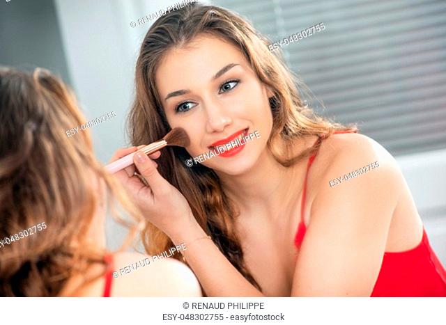 a young smiling woman putting makeup in the mirror
