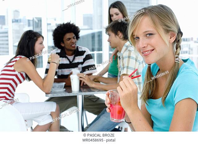 Portrait of a young woman holding a glass of juice in a restaurant with her friends sitting in the background