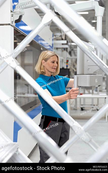 Woman examining machinery seen through railing at factory