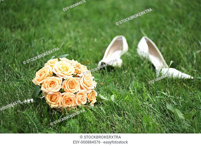 Close-up of bridal yellow rose bouquet on background of her white shoes on green grass