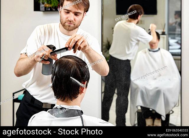 Professional hairdresser does haircut for good looking man at modern barber shop