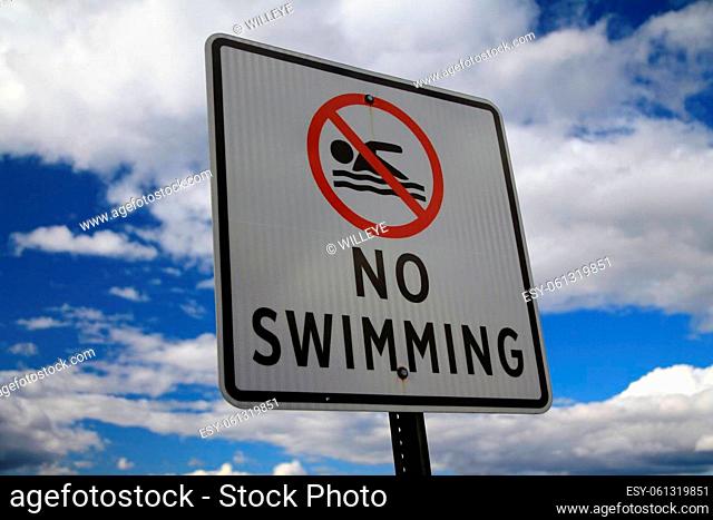 The No Swimming sign with the icon and a blue and white sky behind during a sunny day