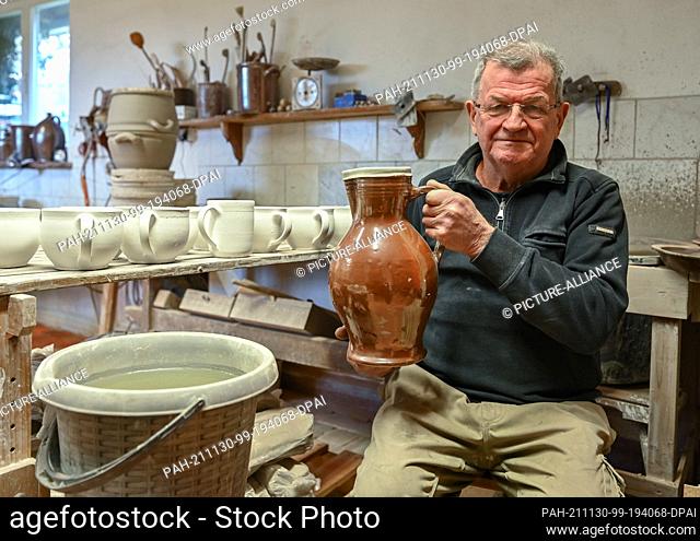 26 November 2021, Brandenburg, Groß Neuendorf: Manfred Dannegger, potter, sits in his workshop holding a jug in his hands