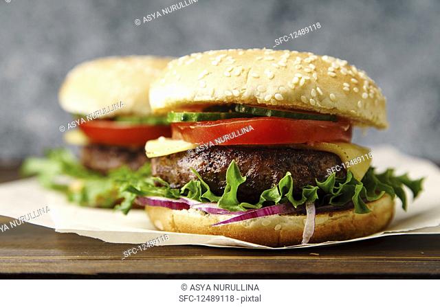 Classical burger with grilled meat, tomatoes, cheese, onion, cucumber and lettuce served on wooden table